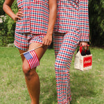 Close up of models wearing the Short Sleeve and Long Sleeve Pajama Set in Patriotic Gingham while holding a flag and Coca-cola 6-pack 