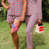 Close up of models wearing the Short Sleeve and Long Sleeve Pajama Set in Patriotic Gingham while holding a flag and Coca-cola 6-pack 