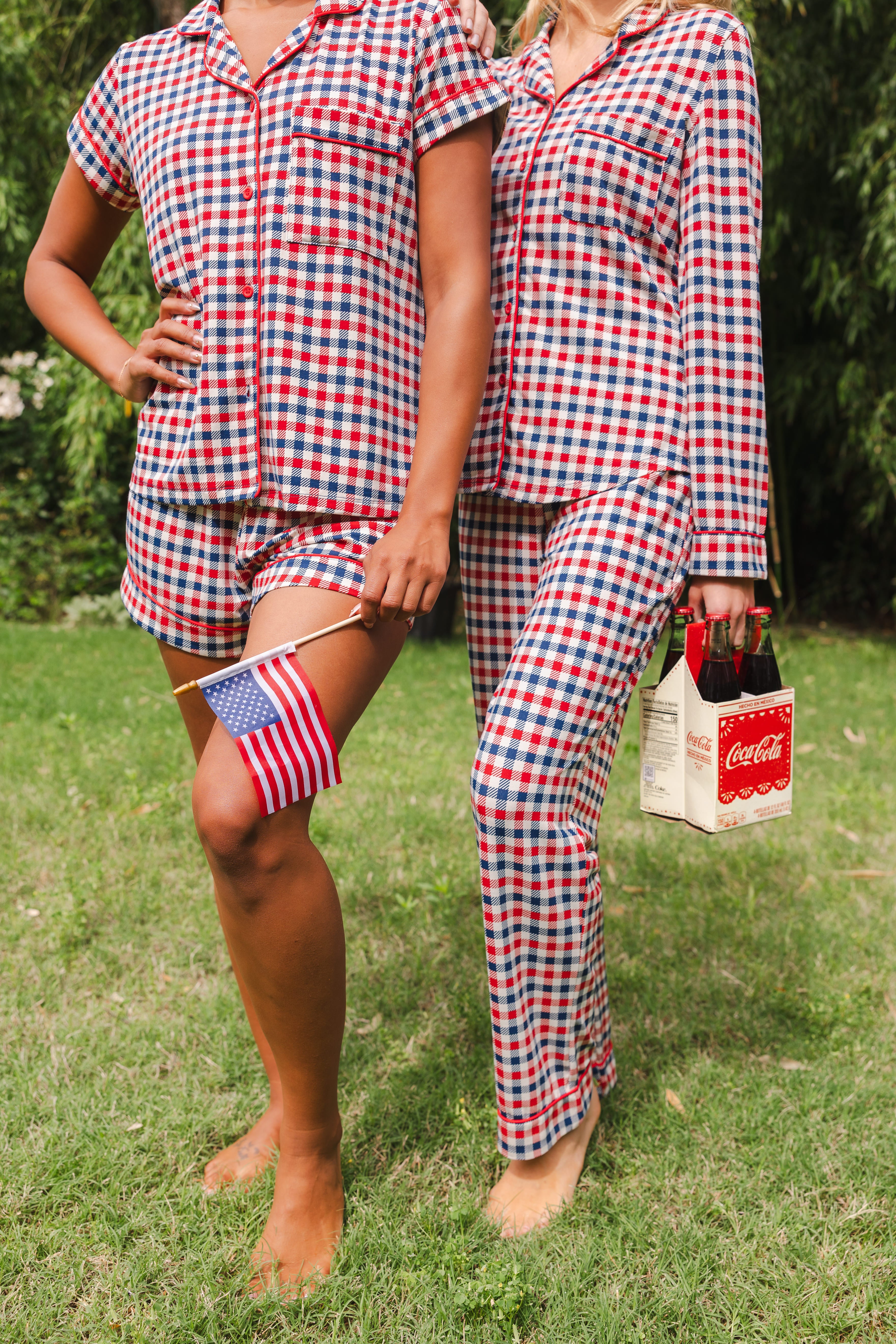 Close up of models wearing the Short Sleeve and Long Sleeve Pajama Set in Patriotic Gingham while holding a flag and Coca-cola 6-pack 