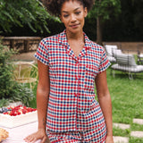Model standing outside next to a picnic table while wearing the Women's Short Sleeve Pajama Set in Patriotic Gingham  ::: Model is 5'9"" wearing size S ///