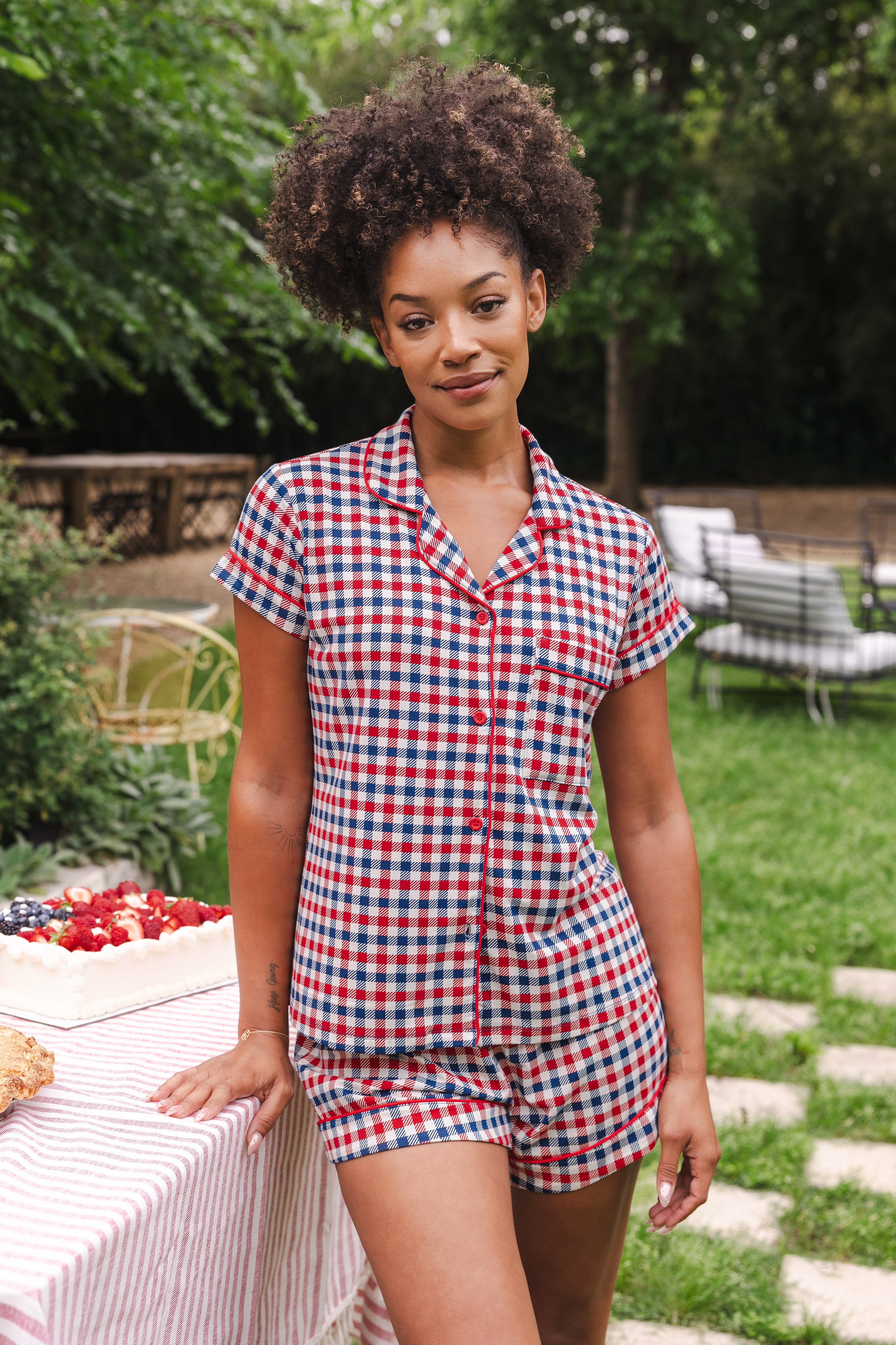 Model standing outside next to a picnic table while wearing the Women's Short Sleeve Pajama Set in Patriotic Gingham  