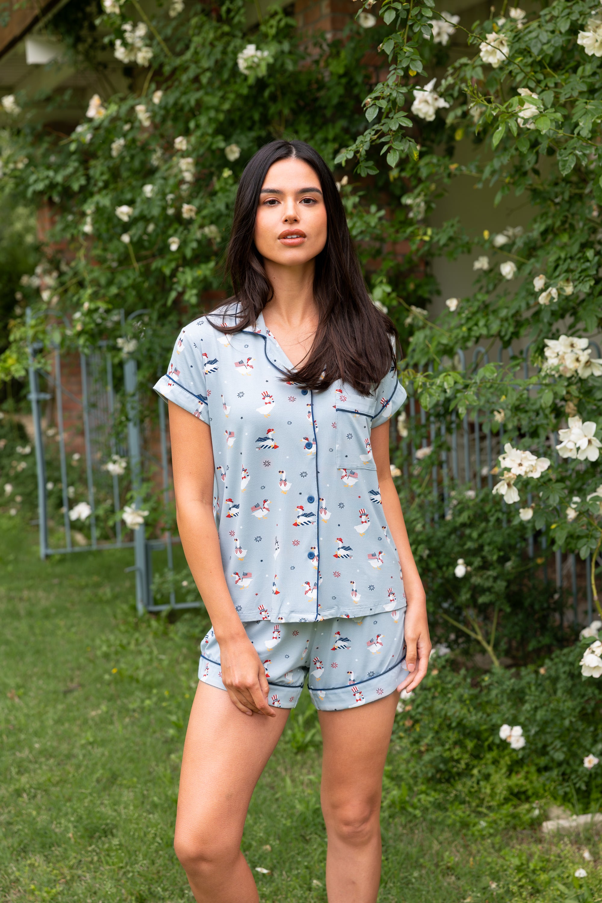 Woman standing in front of greenery and white flowers while modeling the Women's Short Sleeve Pajama Set in Patriotic Goose

