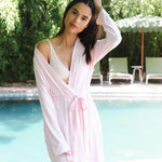 Woman in a pink robe standing by a pool with greenery in the background