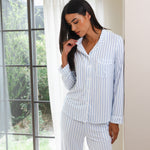 Woman wearing a light blue and white striped pajama set standing by a window.