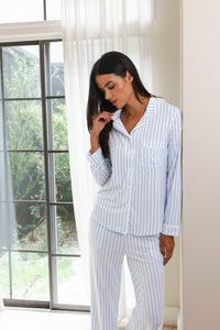 Woman wearing a light blue and white striped pajama set standing by a window.