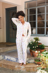 Woman in a white tulip pajama set standing on a porch with potted plants.