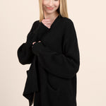 Model wearing black chunky knit oversized cardigan over a silk dress