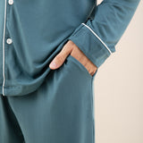 Man modeling button up long sleeve pajamas in a teal blue color with white trim close up on pant pocket detail