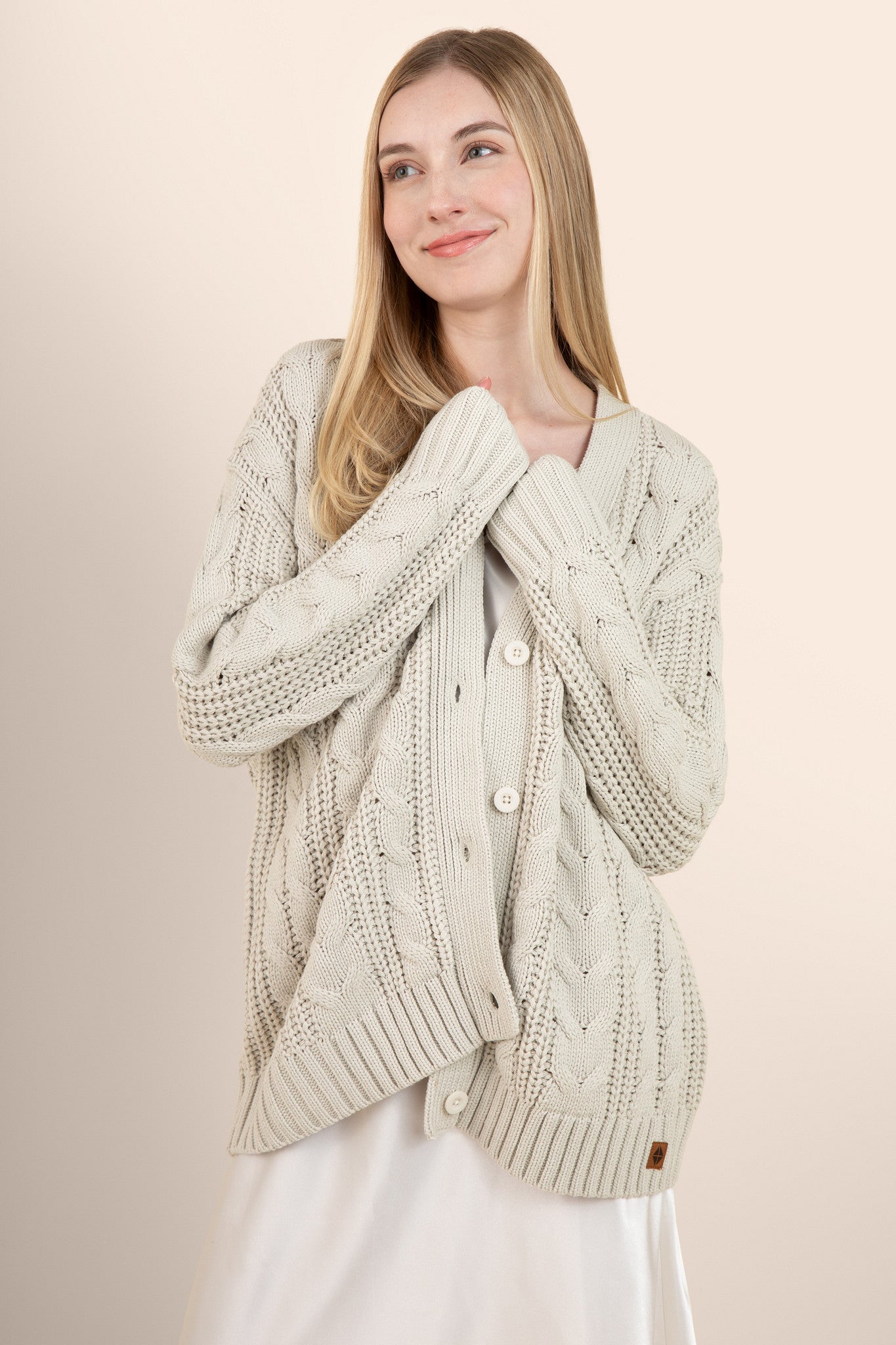 Woman modeling oat colored cable knit cardigan over a silk dress  