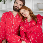 Couple wearing red pajamas with candy cane patterns sitting on a couch.