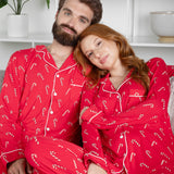 Couple wearing red pajamas with candy cane patterns sitting on a couch.