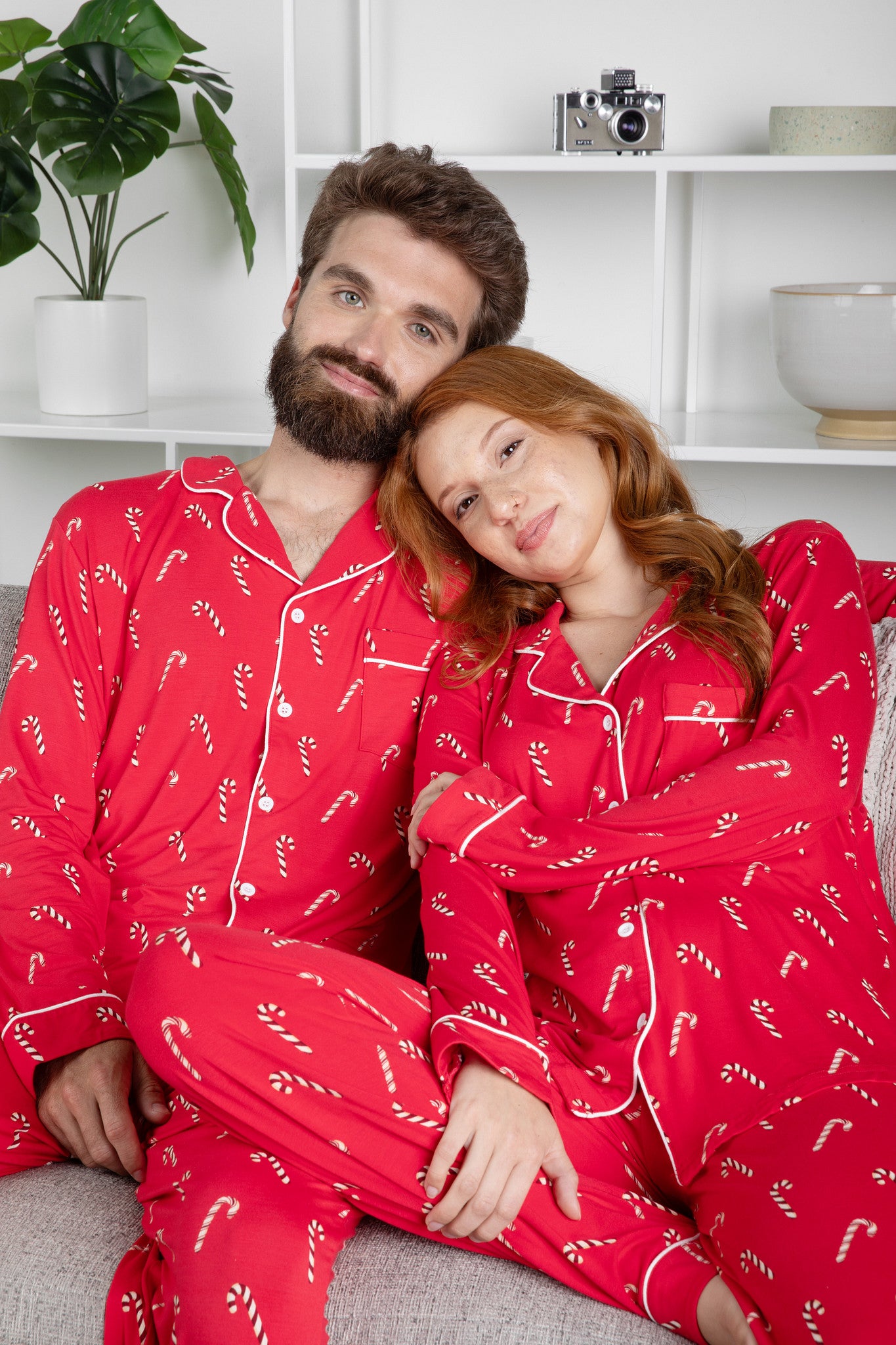 Couple wearing red pajamas with candy cane patterns sitting on a couch.
