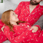 Man and woman wearing red pajamas with candy cane patterns sitting on a couch.