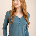 Woman wearing a teal long-sleeve top with buttons on a beige background