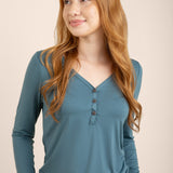 Woman wearing a teal long-sleeve top with buttons on a beige background