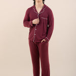 Person wearing burgundy pajamas with white piping on a beige background