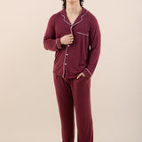 Person wearing burgundy pajamas with white piping on a beige background