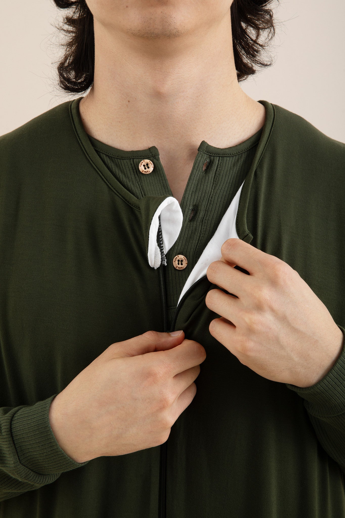 Person wearing a green long-sleeve shirt with buttons, adjusting the collar.