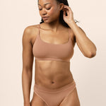 Woman wearing a tan bralette and underwear set on a beige background