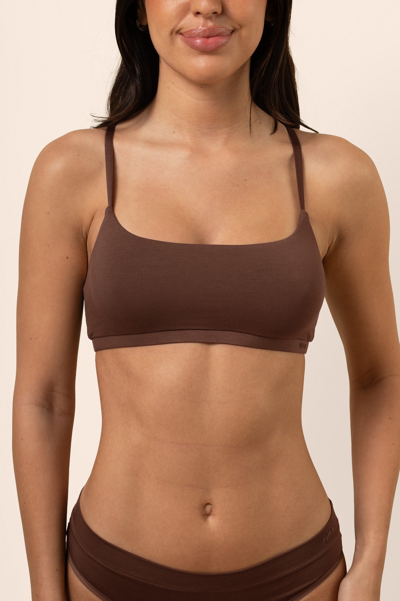 Woman wearing a brown bra and underwear set against a beige background