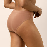 Person wearing a tan bra and panties set on a plain background