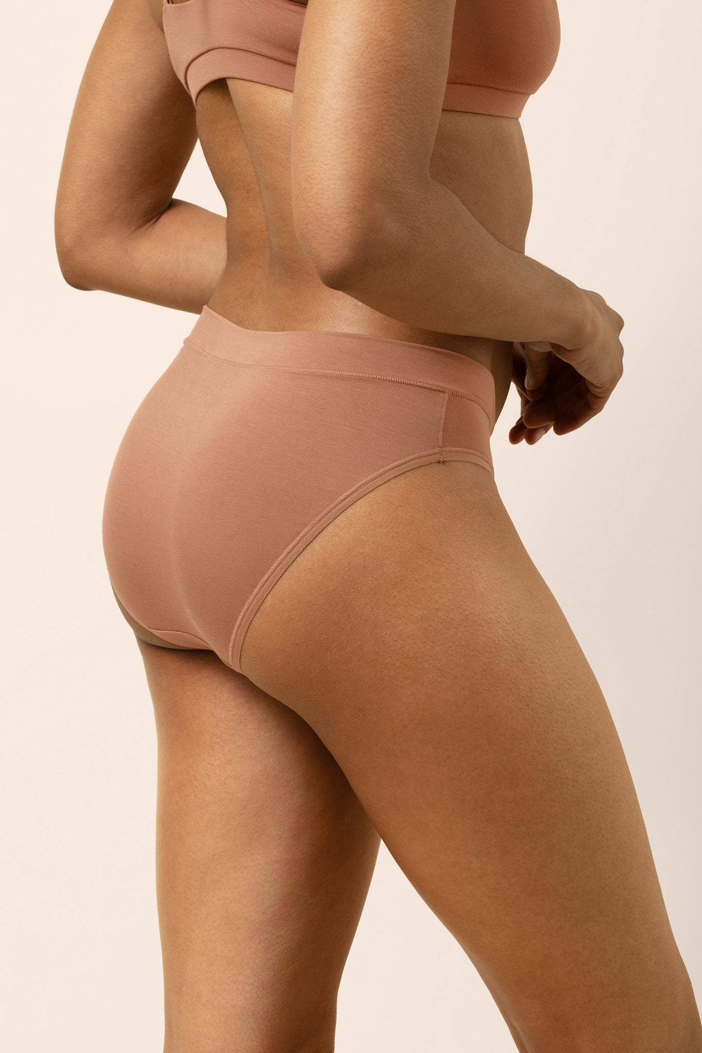 Person wearing a tan bra and panties set on a plain background