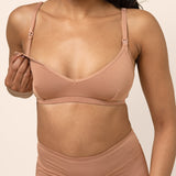Woman wearing a tan bamboo nursing bra showing the clip functionality against a beige background 