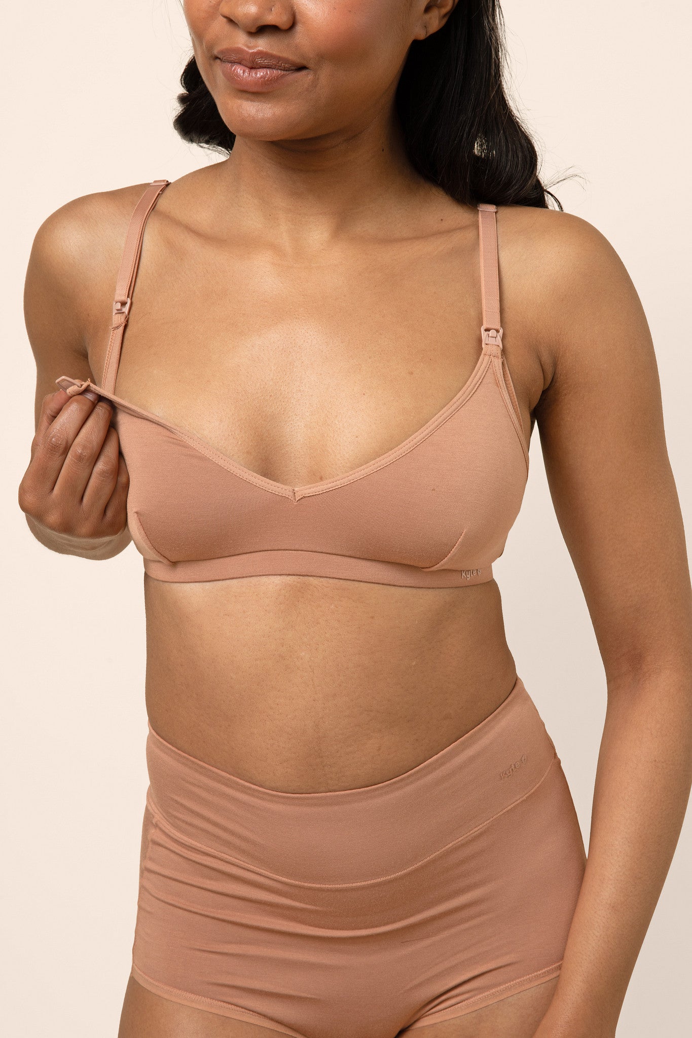 Woman wearing a tan bamboo nursing bra showing the clip functionality against a beige background 