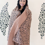 Woman smiling while modeling the Kyte Throw Blanket in Latte Leopard 2.5 TOG
