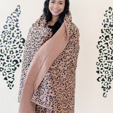 Woman smiling while modeling the Kyte Throw Blanket in Latte Leopard 2.5 TOG