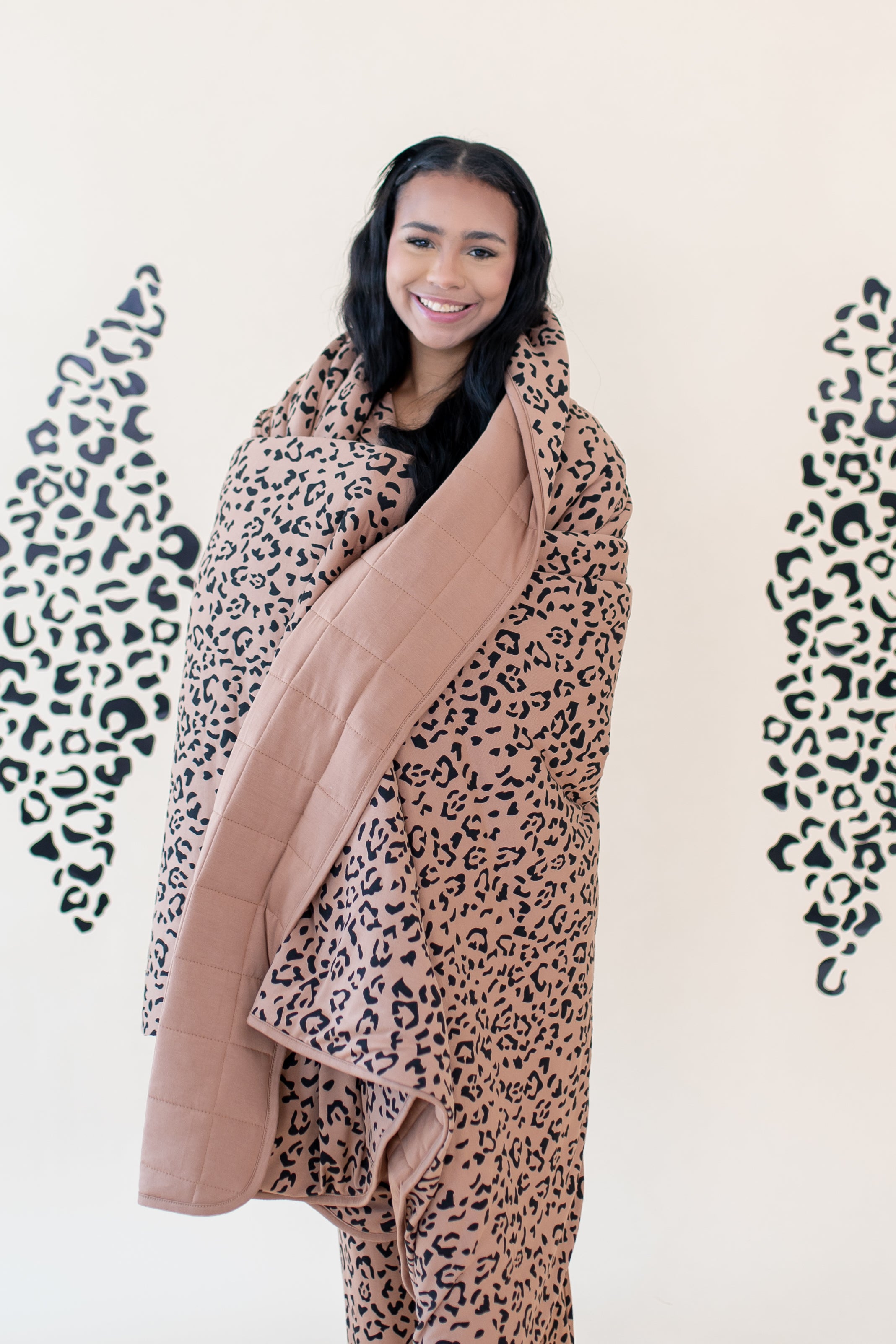 Woman smiling while modeling the Kyte Throw Blanket in Latte Leopard 2.5 TOG