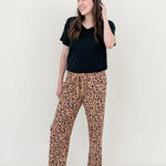Smiling model looking to the side while wearing the Lounge Pants in Latte Leopard paired with a black V Neck