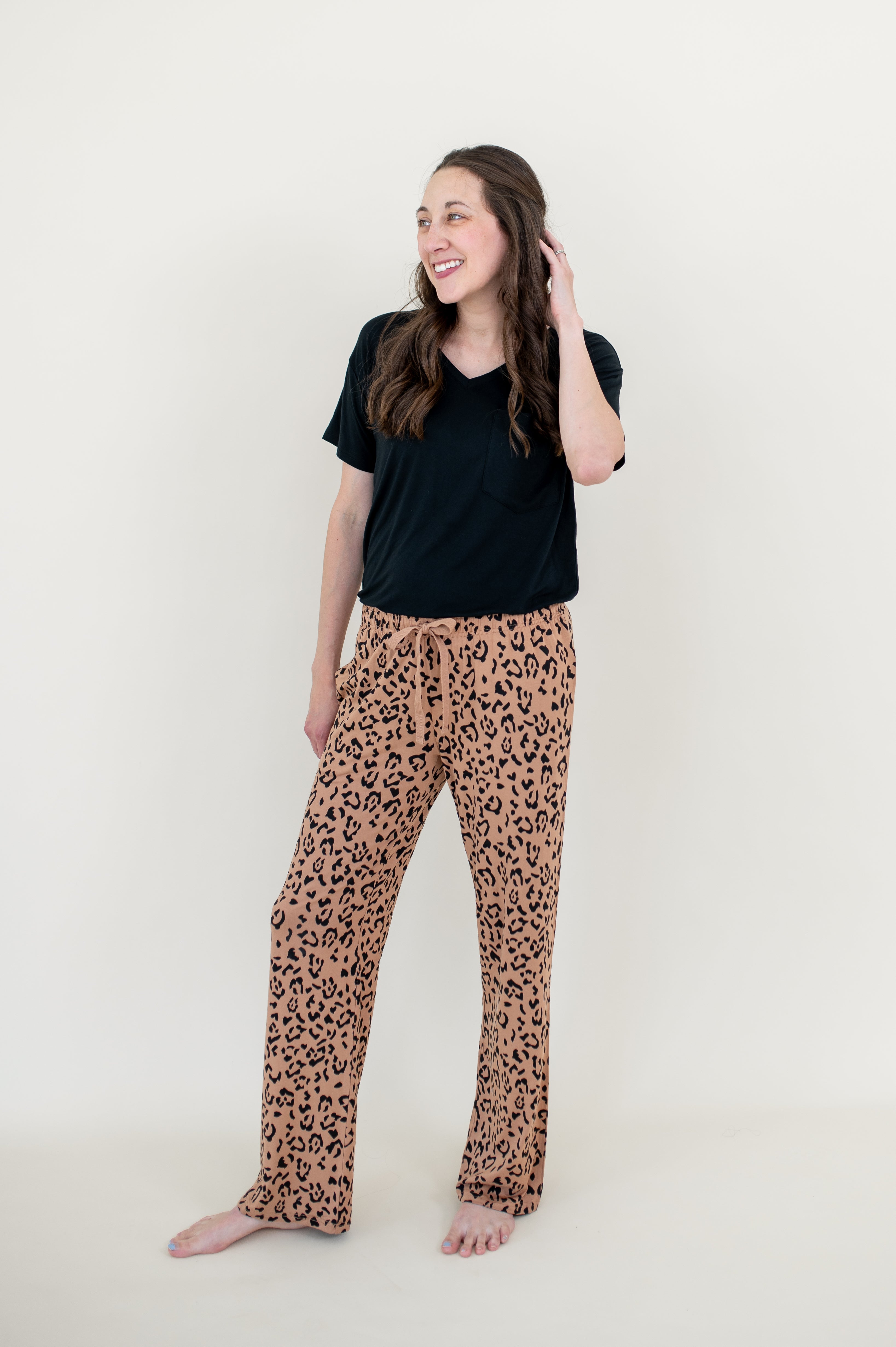 Smiling model looking to the side while wearing the Lounge Pants in Latte Leopard paired with a black V Neck