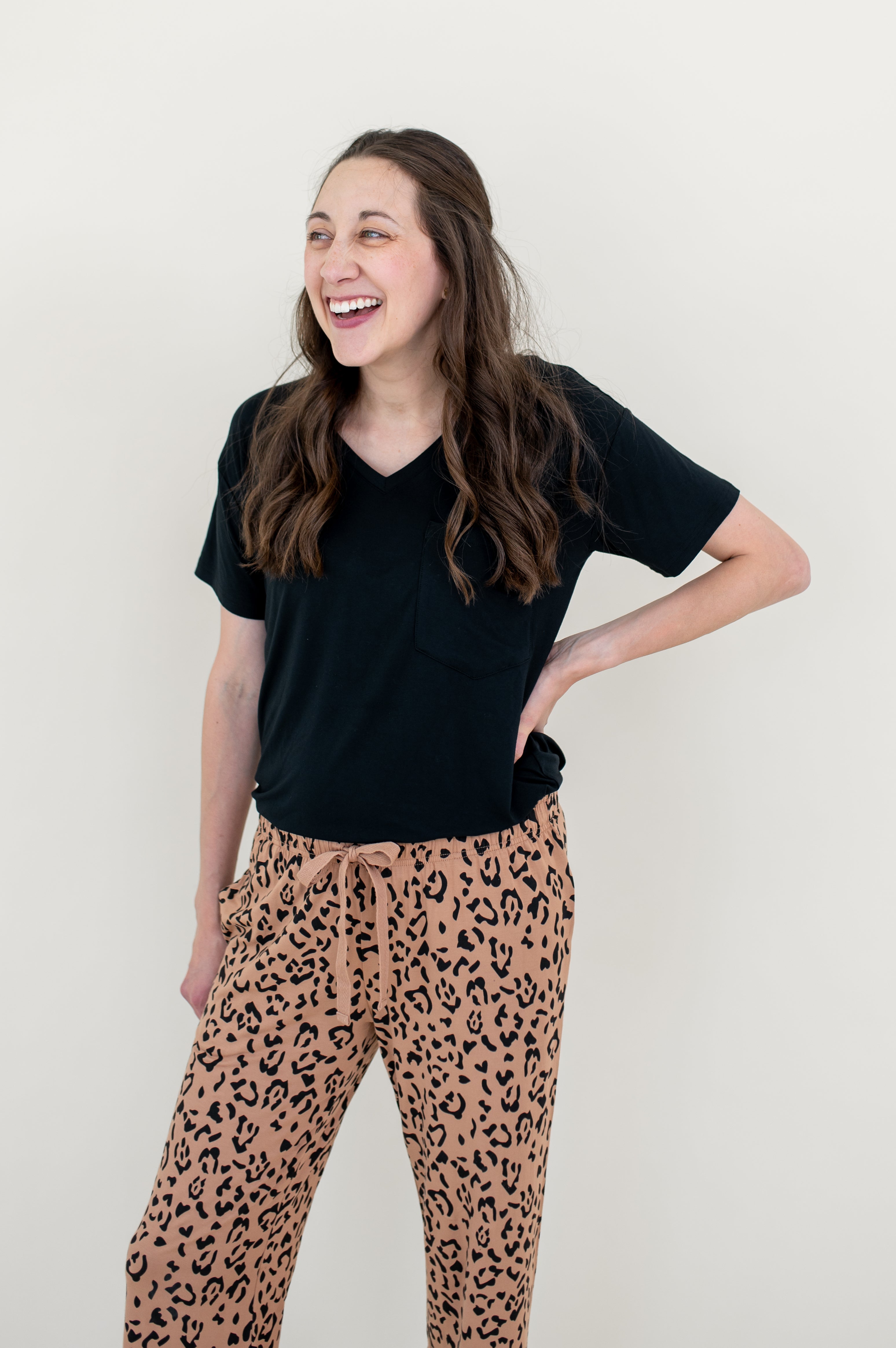 Woman laughing and modeling the Lounge Pants in Latte Leopard paired with a black V Neck