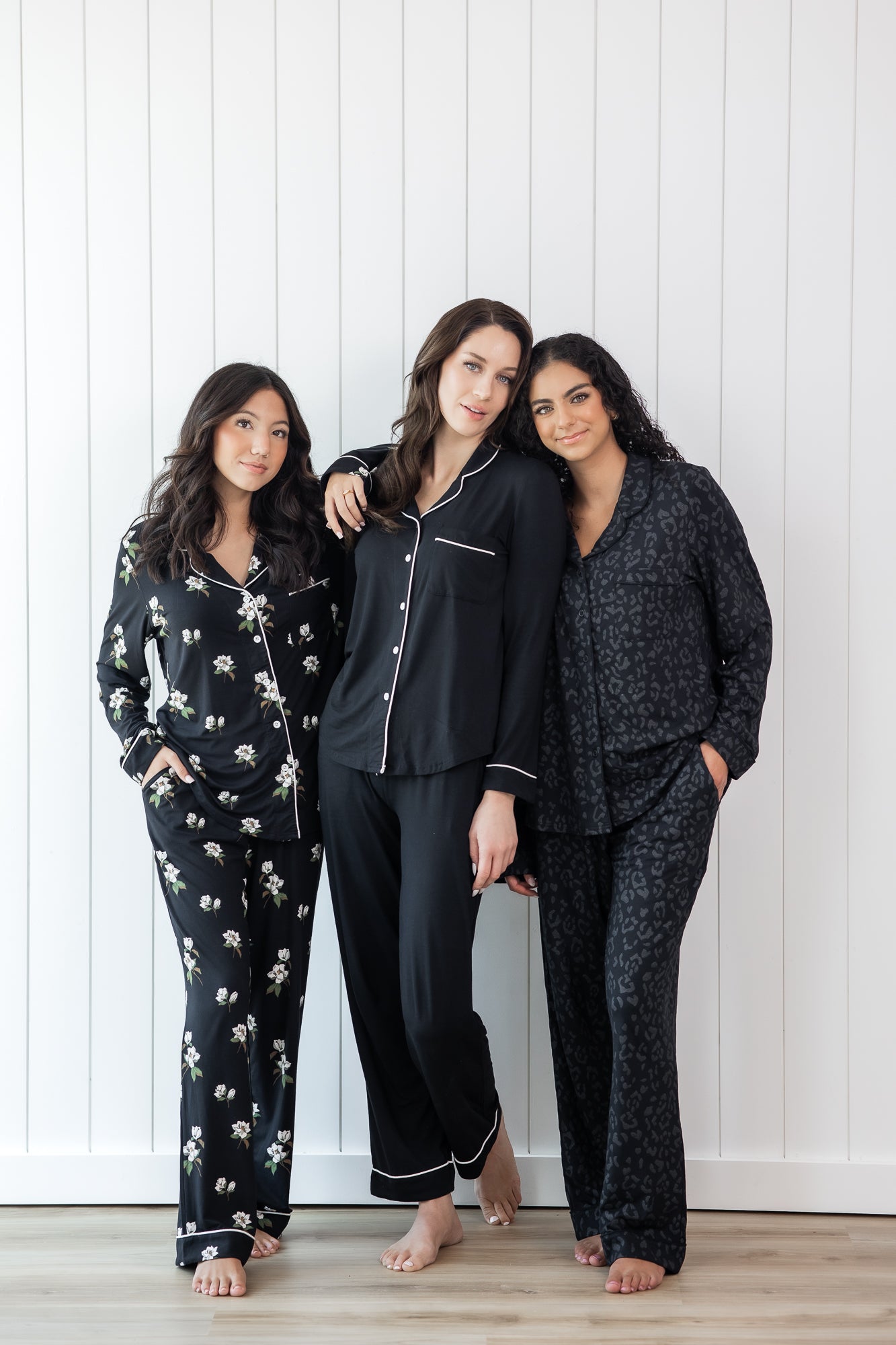 Group of 3 models wearing long sleeve button up pajamas against a white wooden wall 