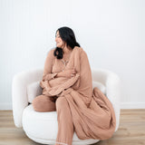 Model with eyes closed and head to the side while wrapped in the Quilt Blanket in Latte 2.5