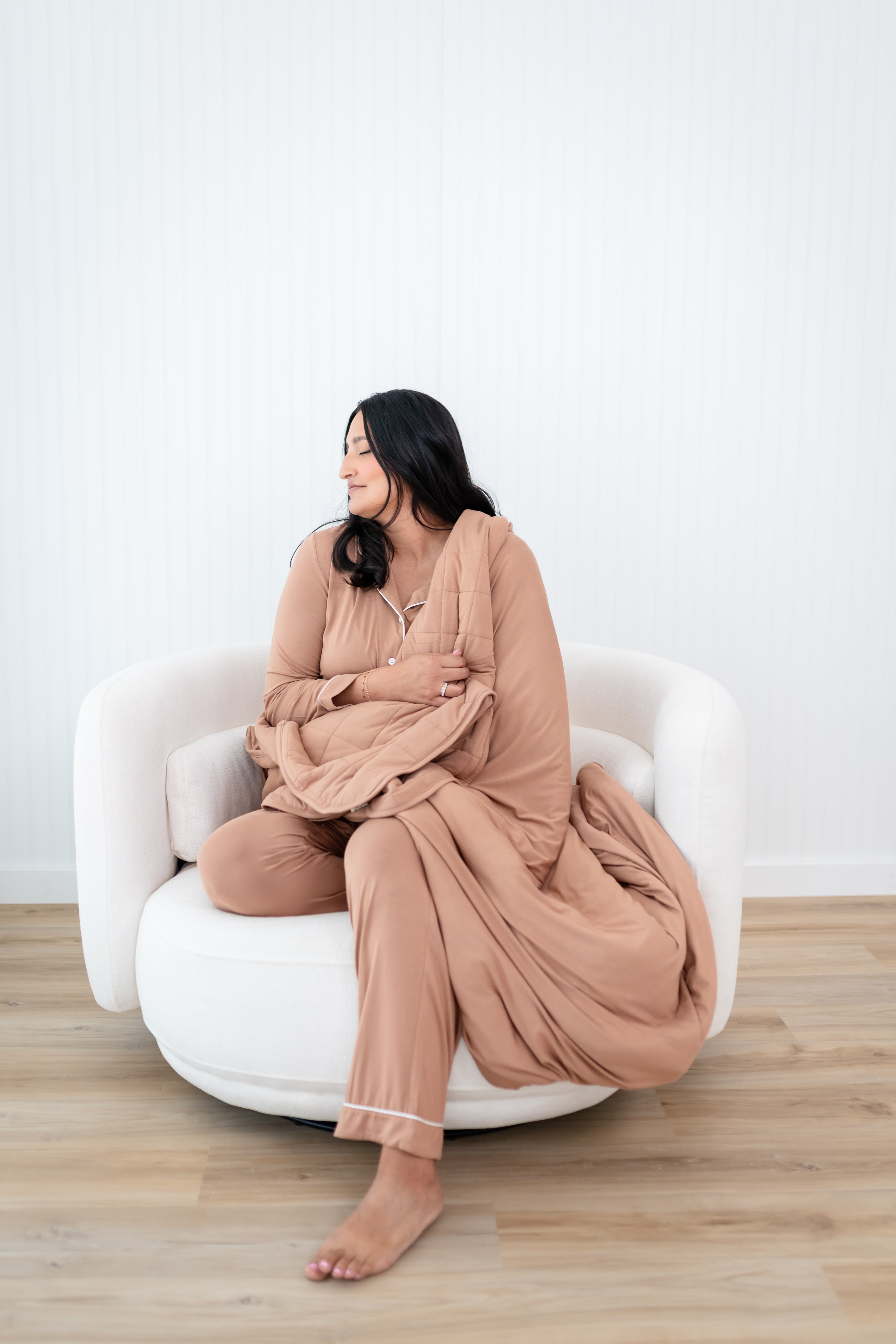 Model with eyes closed and head to the side while wrapped in the Quilt Blanket in Latte 2.5