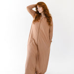 Model with hand in hair while wearing the Kyte Adult Sleep Bag Walker in Latte