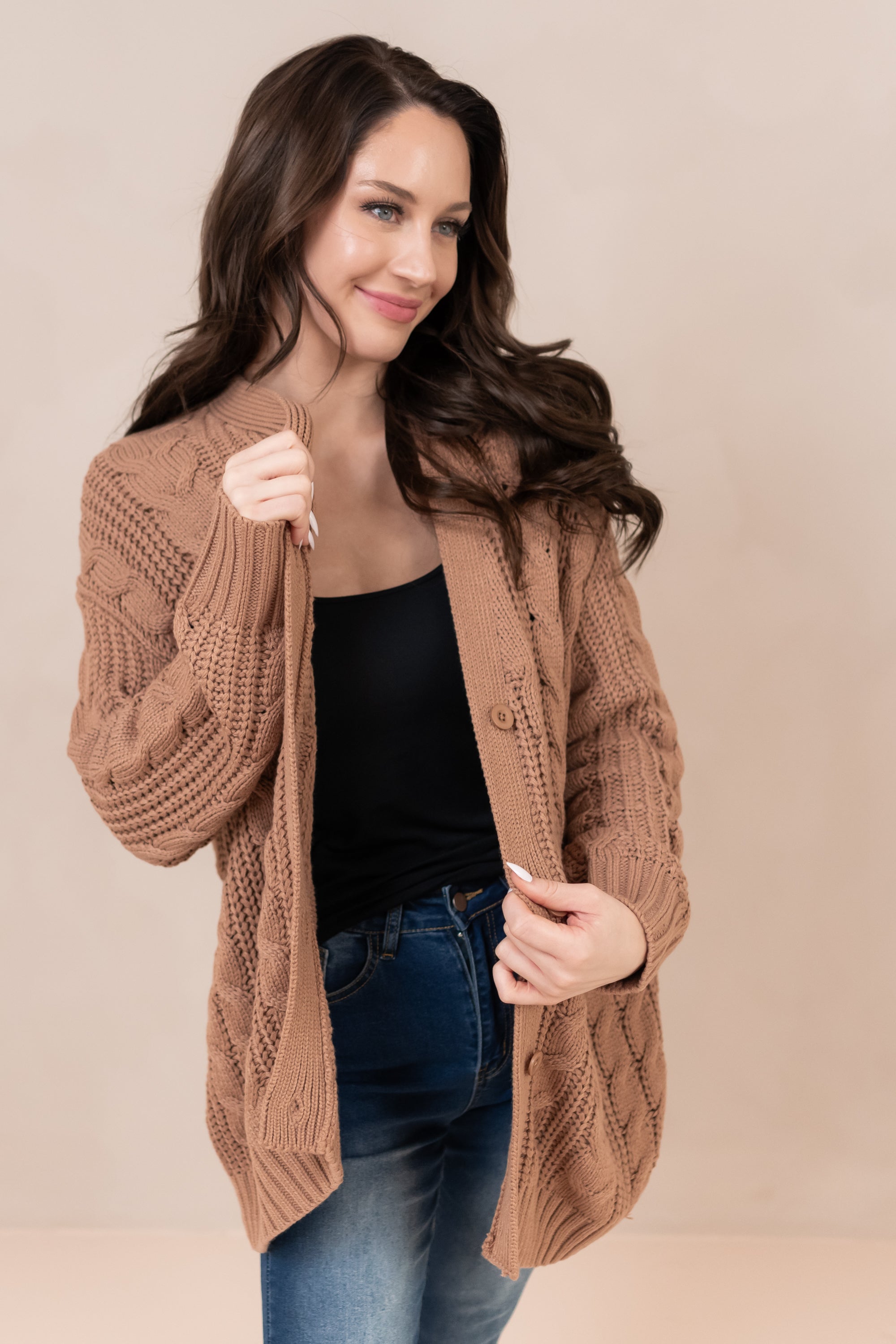 Woman looking to the side while holding on to the Chunky Cable Knit Cardigan in Latte