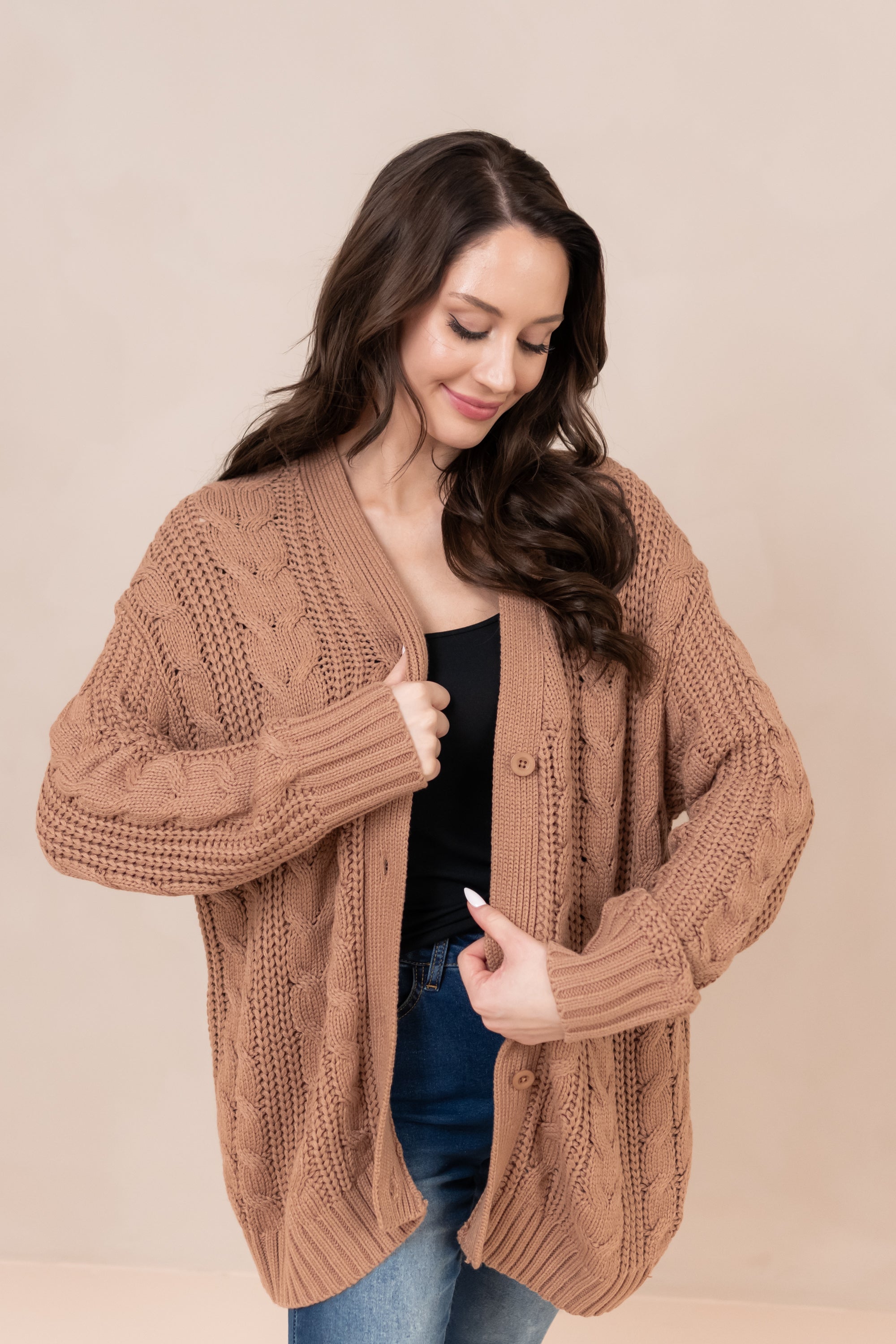 Model smiling downwards wearing the Chunky Cable Knit Cardigan in Latte