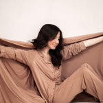 Smiling model holding Bamboo Quilt Blanket in Latte 2.5 open while matching in the Long Sleeve Pajama Set in Latte