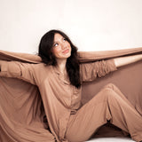 Smiling model wearing the Women's Long Sleeve Pajama Set in Latte while wrapped in the Bamboo Quilt Blanket in Latte 2.5