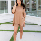 Woman in a beige biker short outfit standing on a patio with glass windows in the background ::: Model is 5'2" wearing size S ///