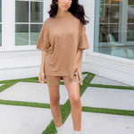 Woman in a beige outfit standing on a patio with a building in the background