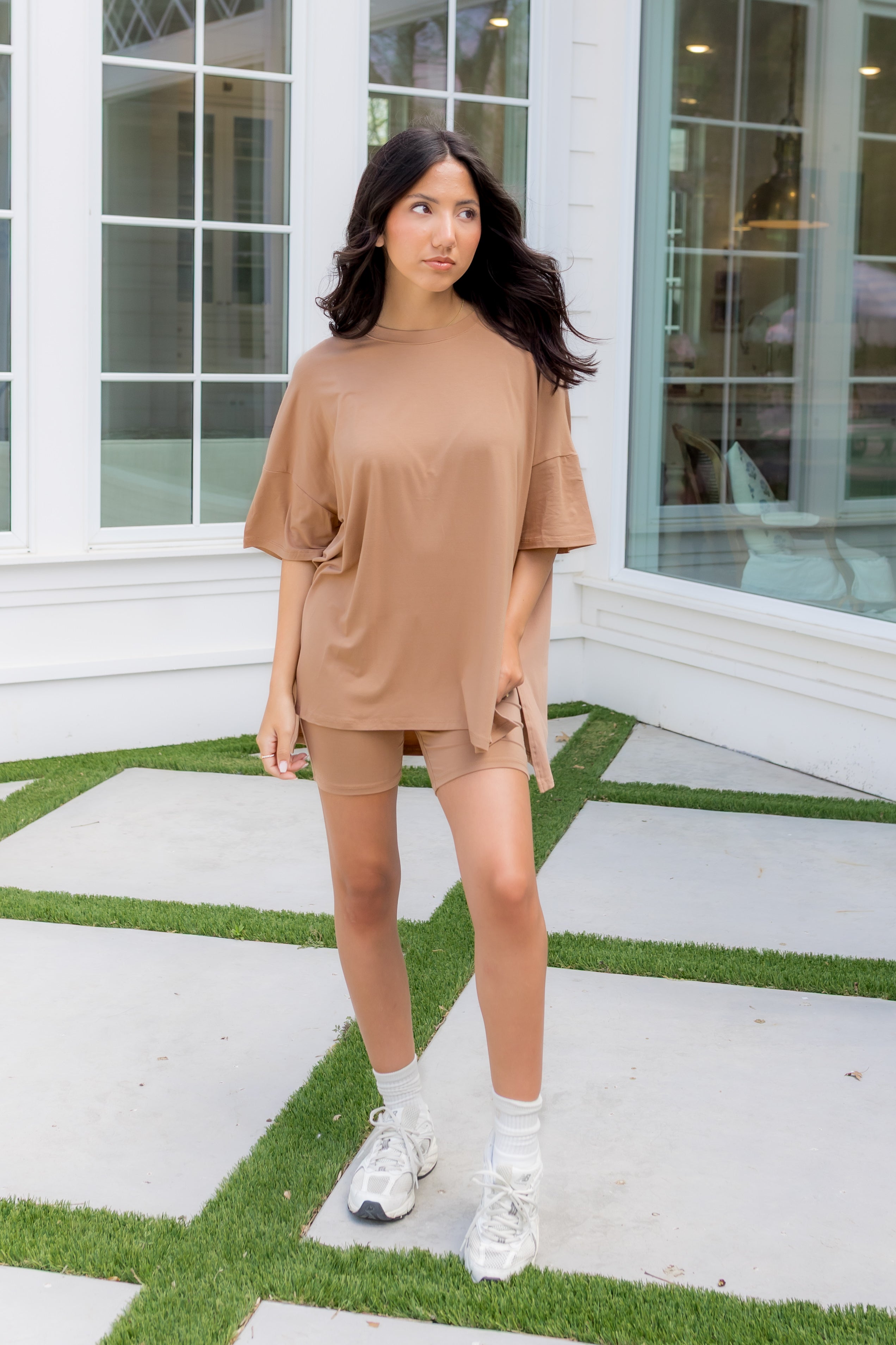 Woman in a beige outfit standing on a patio with a building in the background