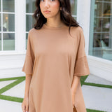 Woman wearing a beige outfit standing in front of a building with large windows.