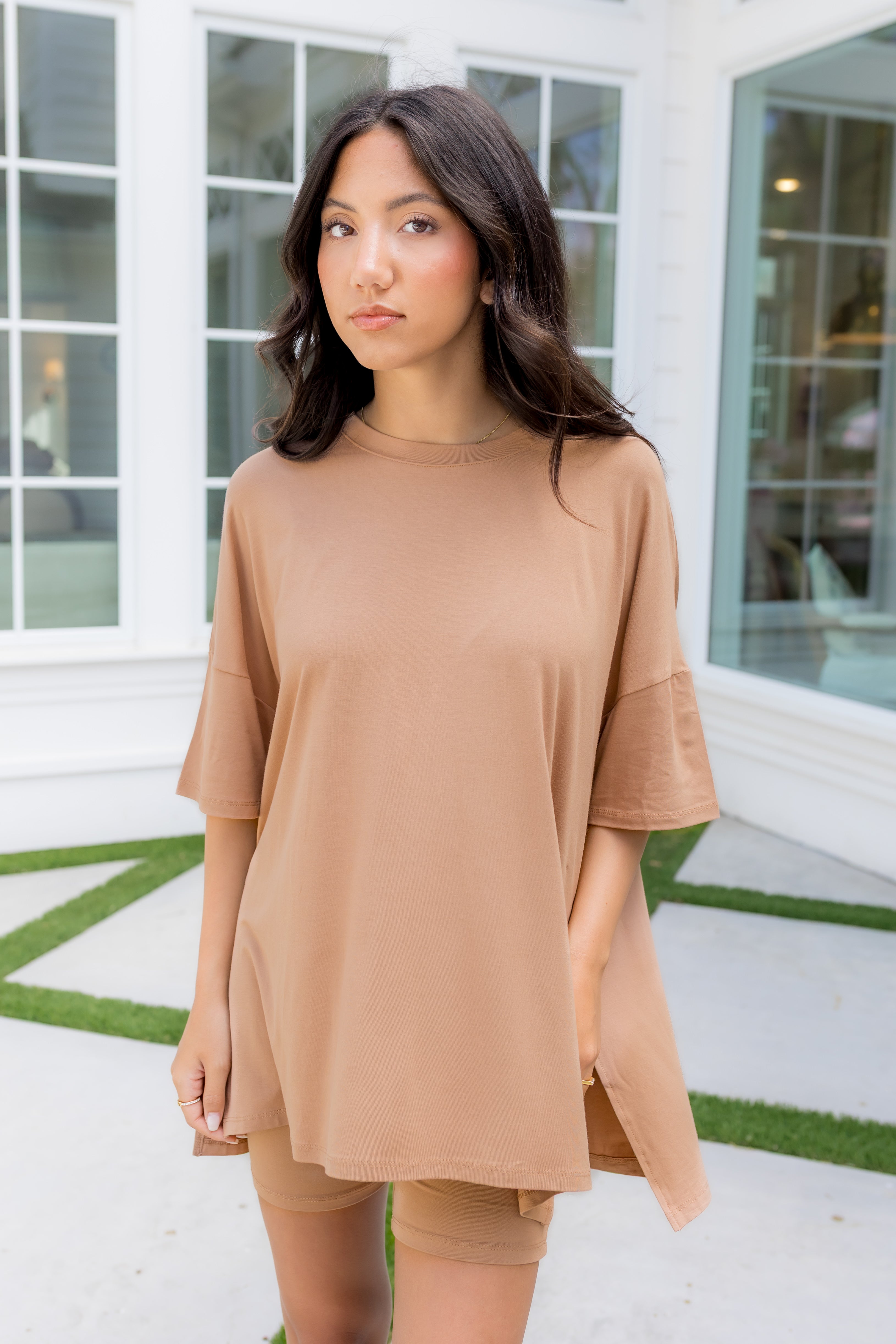 Woman wearing a beige outfit standing in front of a building with large windows.