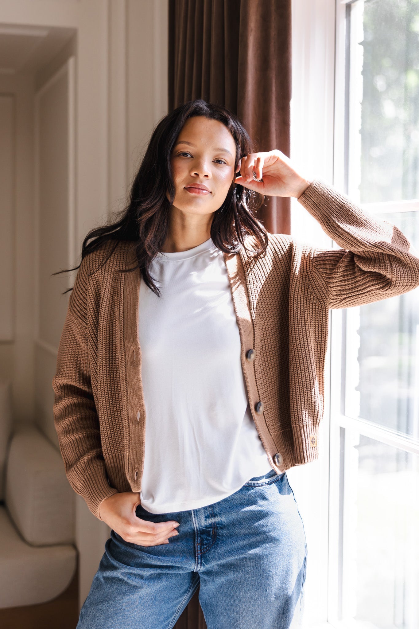 Woman with her arm propped on the window wearing a cropped cardigan in late and jeans
