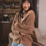 Modal sitting  against a sofa in a living room wearing Chunky Knit Women's Waffle Cardigan in Latte over white camisole and blue jeans
::: Model is 5'9" wearing size S ///