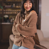 Modal sitting  against a sofa in a living room wearing Chunky Knit Women's Waffle Cardigan in Latte over white camisole and blue jeans
::: Model is 5'9" wearing size S ///